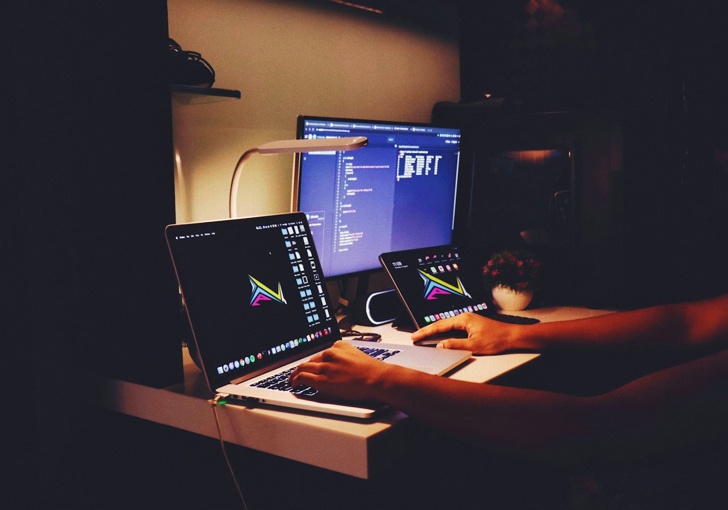 Hands typing on a laptop next to a tablet on a desk.