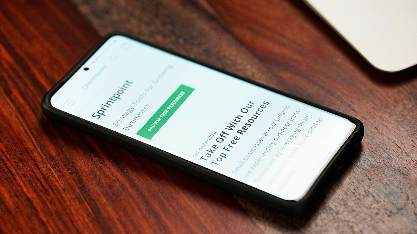 Smartphone displaying Sprintpoint business website on wooden table.